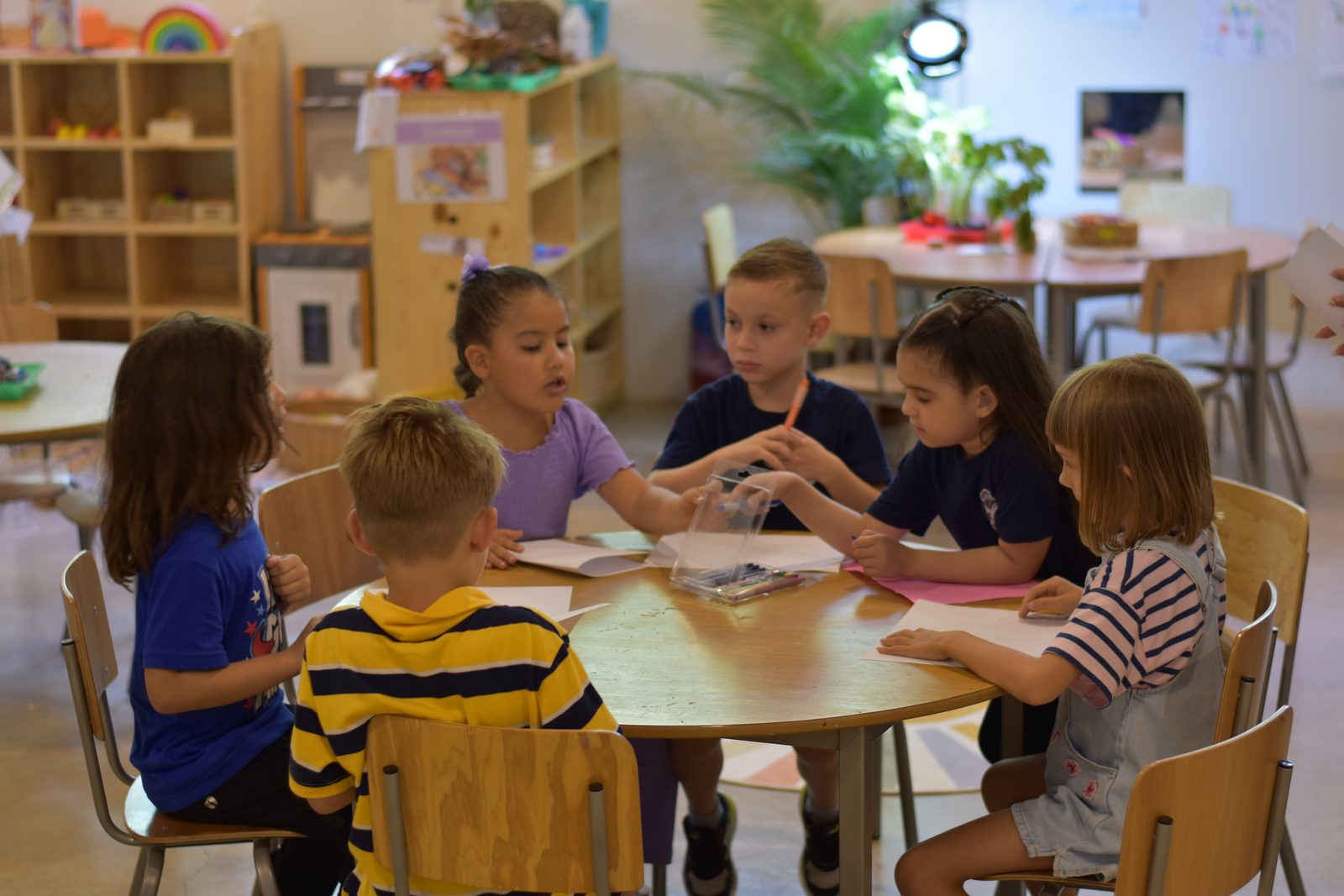 Young children gathered around a wooden table in a bright classroom