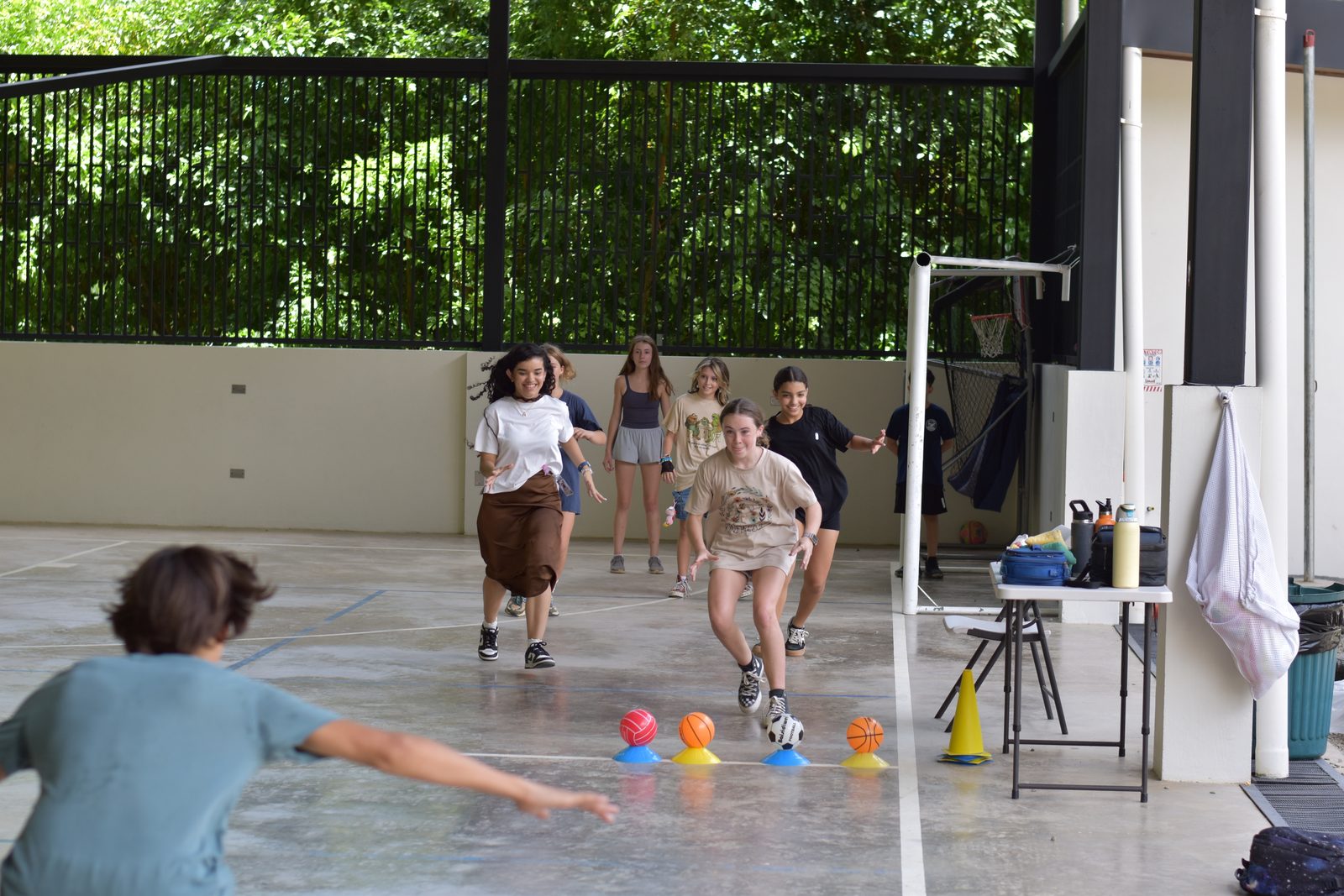 Students running during relay race with colorful balls on gymnasium floor