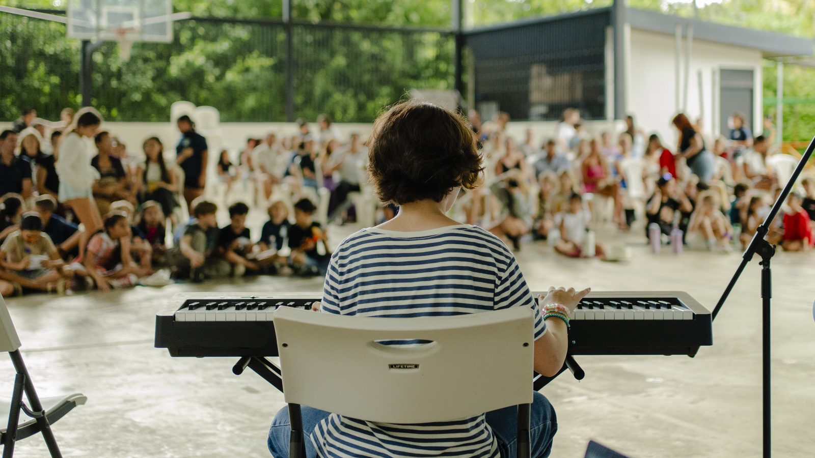 Musician plays keyboard before seated students gathered in large open courtyard