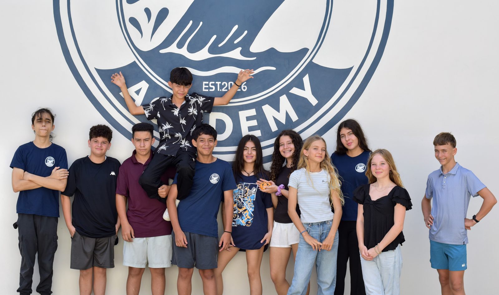 Group of elementary and middle school students in casual clothing pose together against white wall
