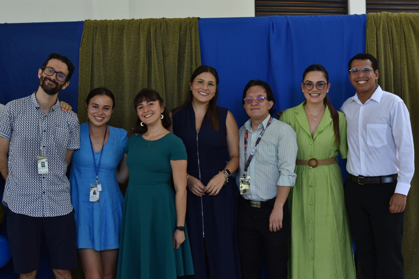 Seven school staff members stand together against blue and green backdrop