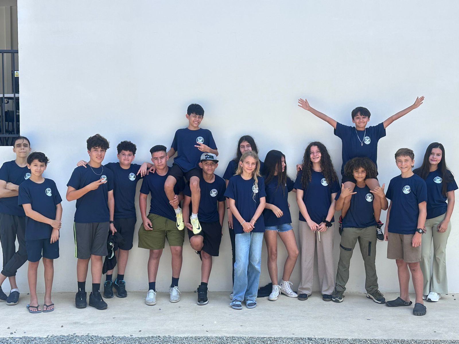 Twelve students in navy uniforms stand in line against white wall with celebratory poses