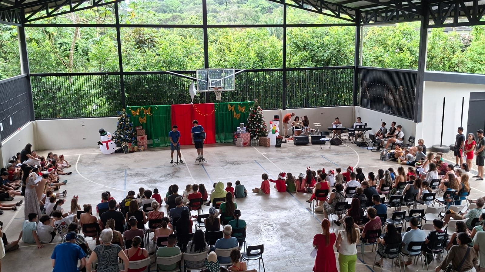 School assembly in covered outdoor structure overlooking jungle with holiday performance on stage