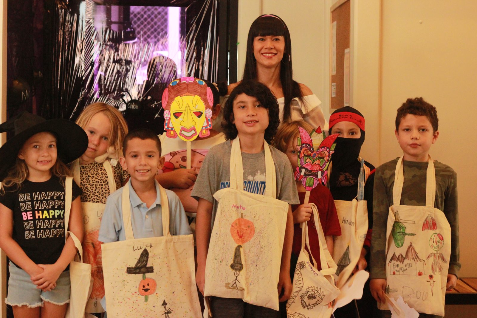 Children display handmade decorative bags with adult in vibrant setting with carnival masks