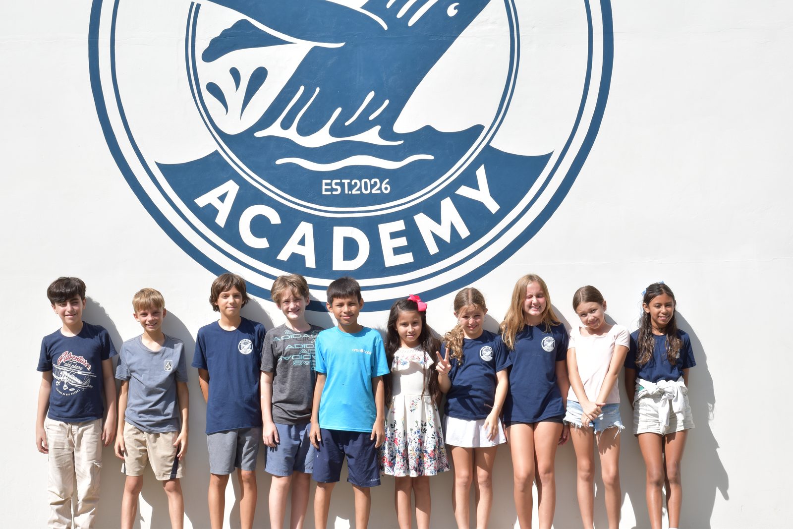 Group of students stand together in line under Ballena Academy logo