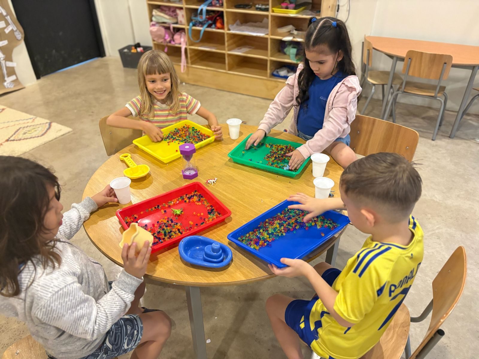 Preschoolers play with colorful beads in sensory trays at a table