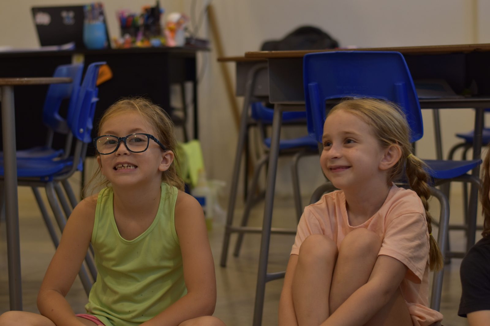 Two students smile in a brightly lit classroom with blue chairs
