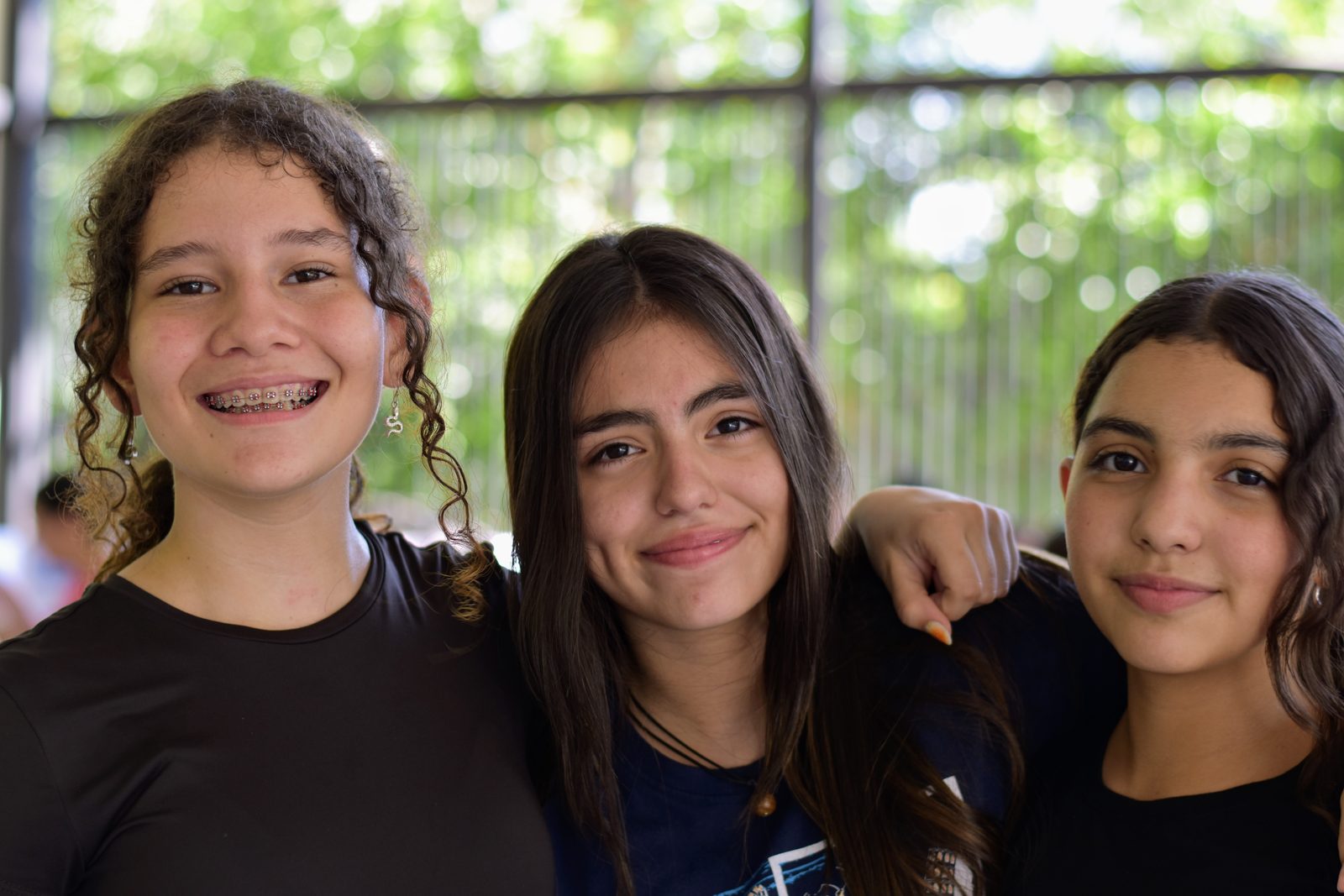 Three smiling secondary students pose together in outdoor setting