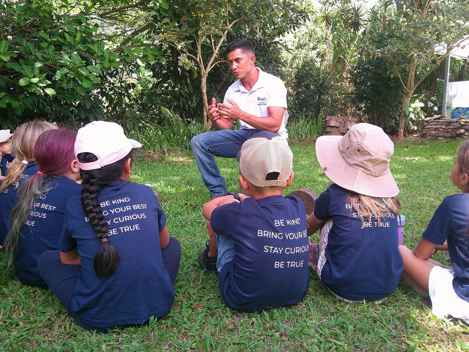 Instructor teaches circle of students seated on grass in jungle