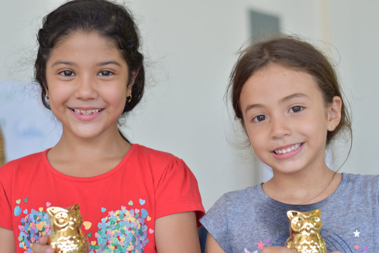 Two girls smiling while holding golden cat figurines