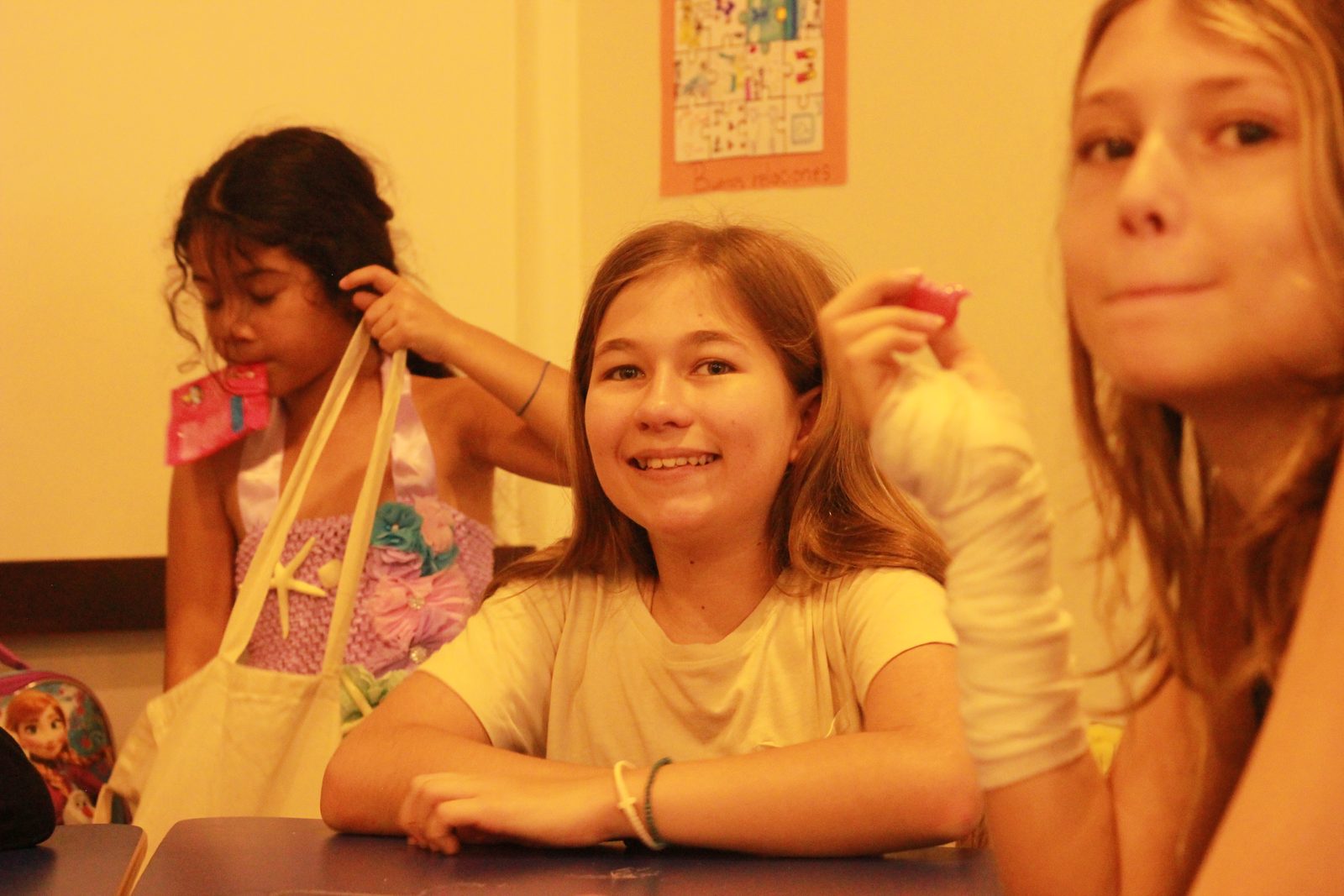 Three girls smiling and playing with fabric ribbons in a classroom