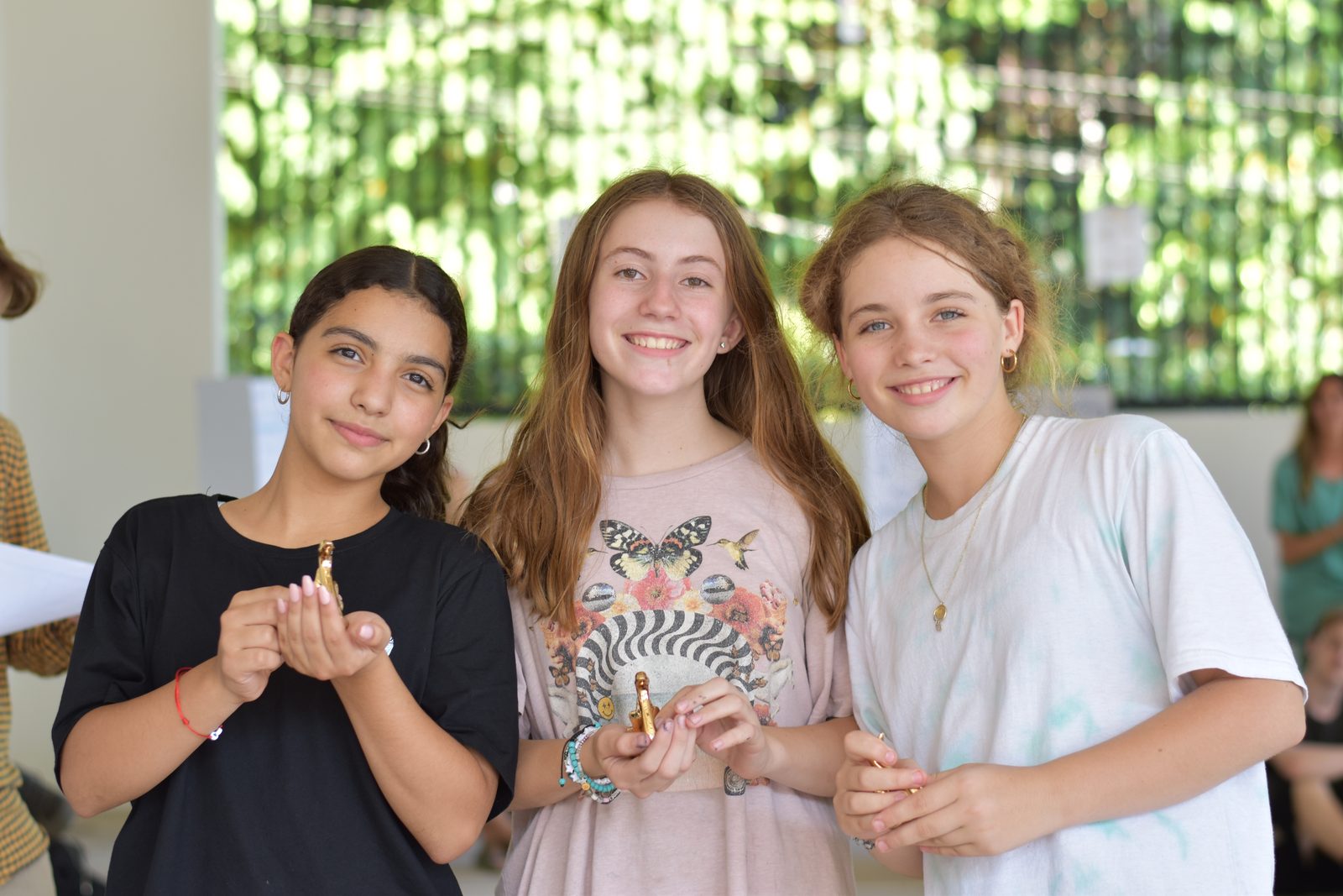 Three smiling girls standing outdoors surrounded by lush green climbing vines
