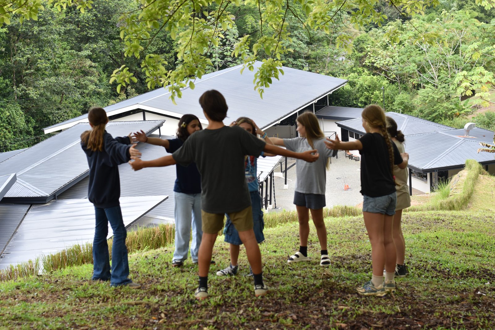 Students hold hands in circle outdoors against jungle backdrop